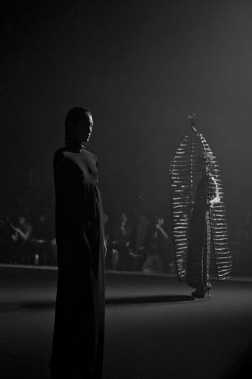 Black and white photography of two models on the runway on has a cage around her in Christian Dada Spring 2012 Collection show during tokyo Fashion week