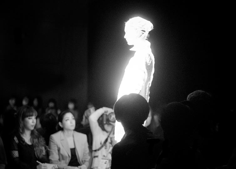 Black and white phot of a glowing model bandaged in knits walking in Johan Ku spring 2012 glow in the dark runway show tokyo fashion week photo by artist danny roberts