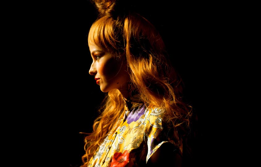 Close up of a the profile of a girl model face with large red hair and a yellow ornate dress in Motonari Ono Spring 2012 collection in Tokyo Japan Fashion week